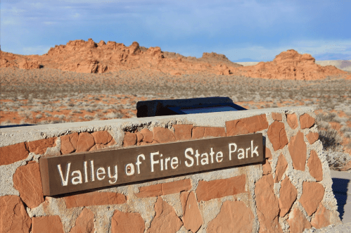 Sign for Valley of Fire State Park with red rock formations and desert landscape in the background.