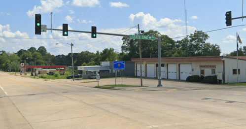 Intersection with traffic lights, a sign for State Line, and buildings in a small town under a blue sky.