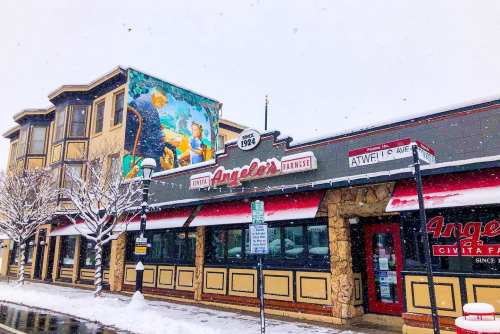 A snowy scene of Angelo's restaurant with a colorful mural on the side, showcasing a winter atmosphere.