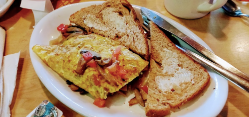 A plate with a mushroom and tomato omelette, served with two slices of toasted bread and a knife.