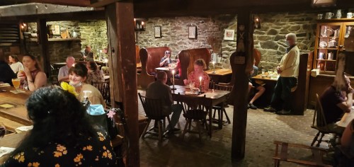 A cozy restaurant interior with stone walls, wooden furniture, and patrons enjoying meals and drinks at tables.