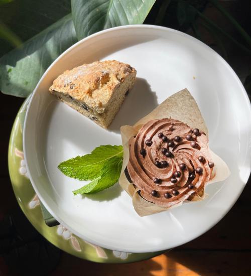 A plate with a scone and a chocolate cupcake topped with chocolate sprinkles, garnished with a mint leaf.