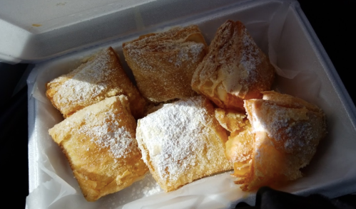 A container filled with golden, flaky pastries dusted with powdered sugar.