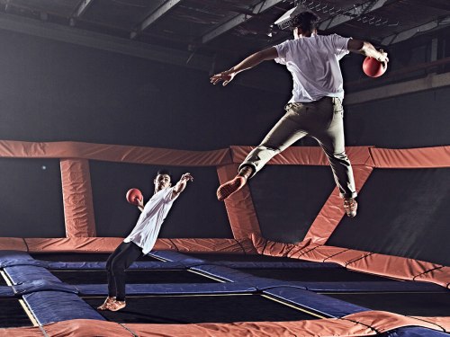 Two people playing dodgeball on a trampoline, one jumping high while the other prepares to throw a ball.