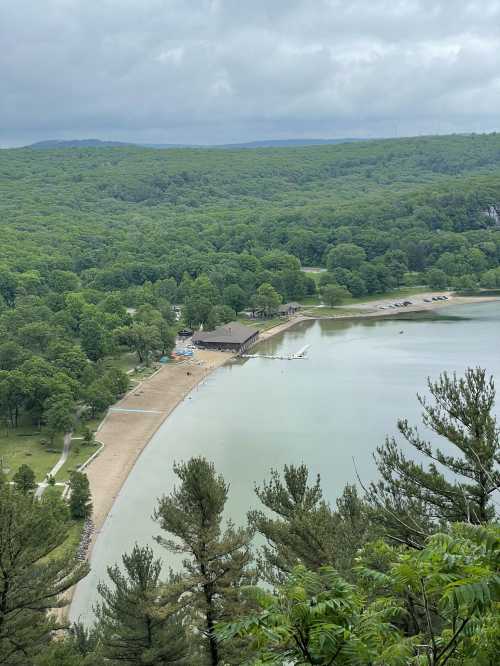 Aerial view of a serene lake surrounded by green trees, with a sandy beach and a building near the water's edge.