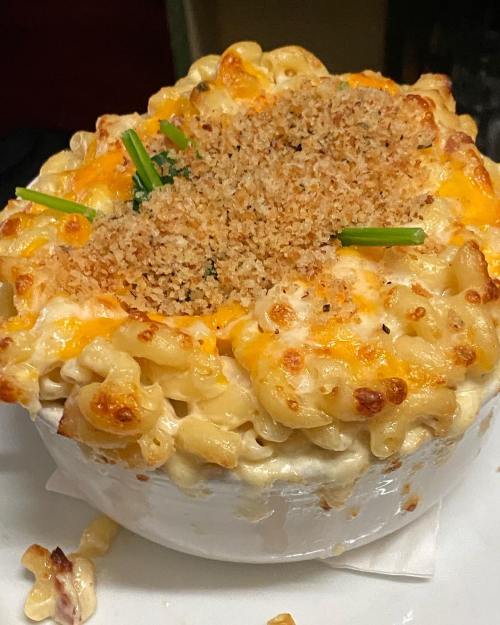 A creamy baked macaroni and cheese dish topped with golden breadcrumbs and green onions, served in a white bowl.