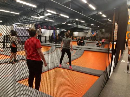 A trampoline park with people jumping and playing on orange trampolines surrounded by safety nets.