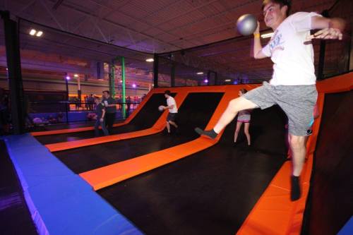 A group of people playing dodgeball on a trampoline court with vibrant lighting and orange and black surfaces.