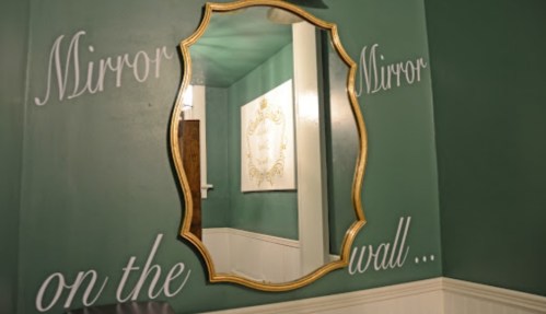A decorative mirror on a green wall with the phrase "Mirror, Mirror on the wall..." written beside it.