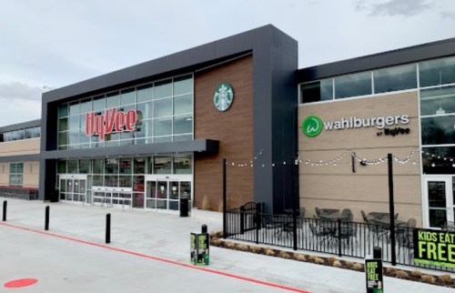 Exterior view of a Hy-Vee grocery store featuring a Starbucks and Wahlburgers, with outdoor seating and signage.