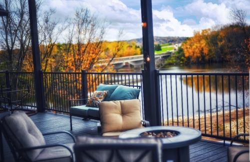 A cozy outdoor seating area with a fire pit, overlooking a river and autumn trees under a cloudy sky.