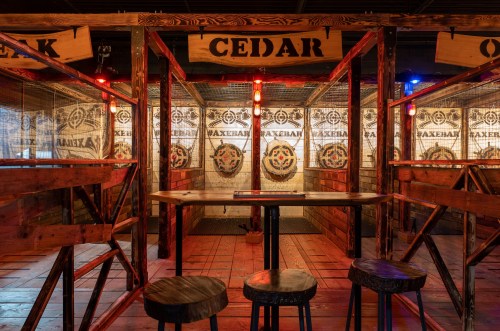 A rustic axe-throwing venue with wooden booths, targets, and dim lighting, featuring a central table and stools.