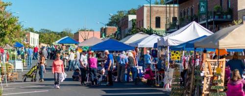 A bustling outdoor market with colorful tents, vendors, and visitors enjoying the sunny day.