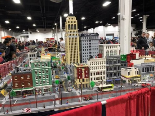 A detailed LEGO city display featuring buildings, streets, and miniature figures at a crowded event.