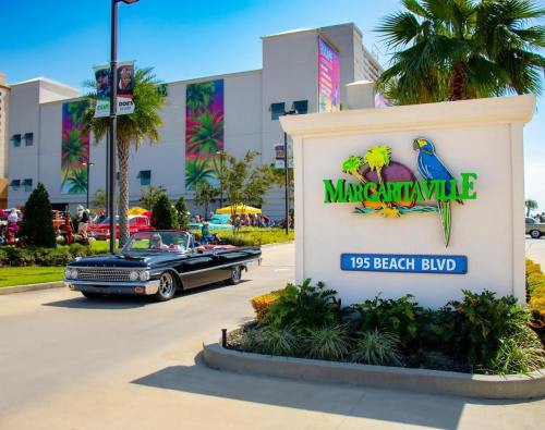 A classic car drives past the Margaritaville sign on Beach Blvd, with colorful buildings and palm trees in the background.