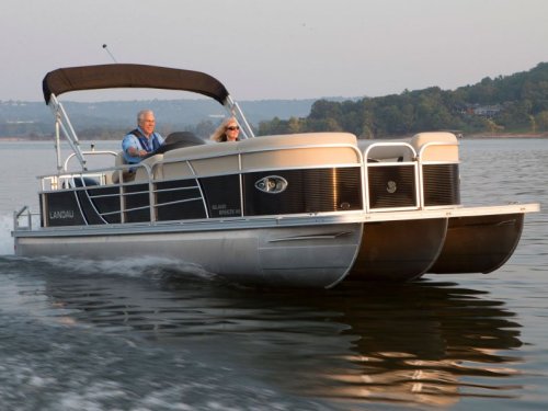 A couple enjoys a leisurely ride on a pontoon boat on a calm lake during sunset.