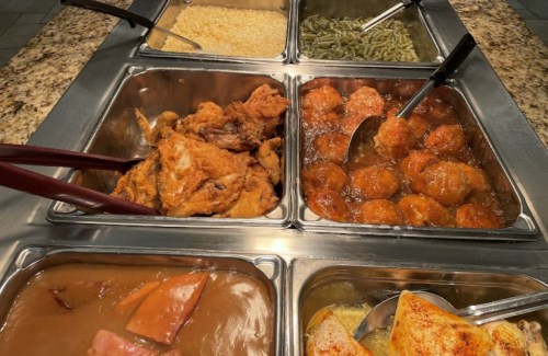 A buffet spread featuring fried chicken, meatballs in sauce, green beans, rice, and a brown gravy dish.