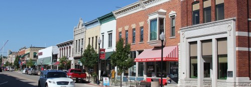 A charming street lined with historic buildings, shops, and trees under a clear blue sky.