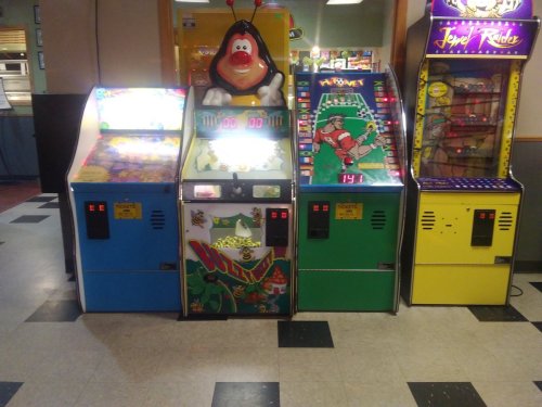 Three vintage arcade machines in a game room, featuring colorful designs and bright screens.