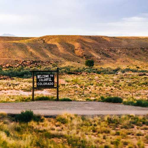 A sign reading "Welcome to Colorful Colorado" in a scenic landscape of rolling hills and grassy fields.