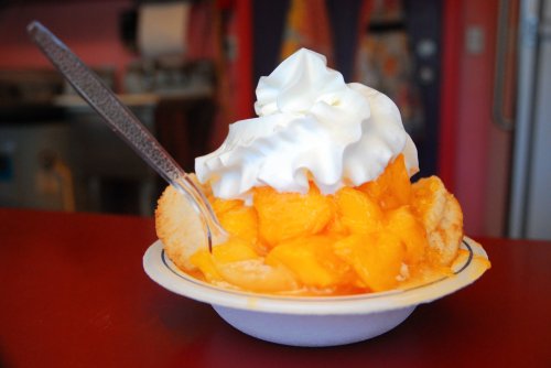 A bowl of peach dessert topped with whipped cream and a spoon, set on a red table.
