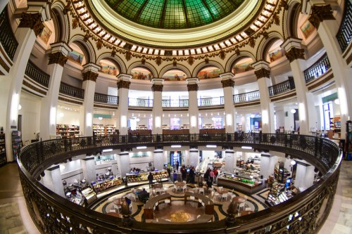 A grand, circular bookstore with a stained glass dome, featuring multiple levels and a café area in the center.