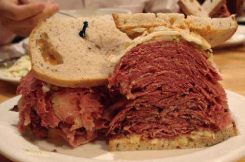 A large sandwich stacked with layers of pastrami and coleslaw, served on rye bread.