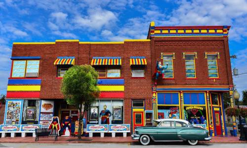 Colorful vintage building with superhero-themed decor and a classic car parked in front under a blue sky.