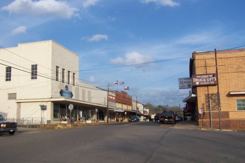 A small town street with shops, flags, and a clear blue sky, showcasing a quaint, rural atmosphere.