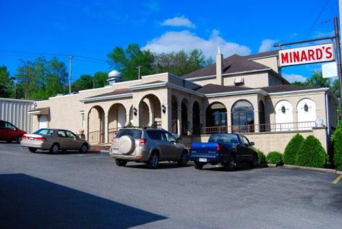 Exterior view of Minard's restaurant, featuring a beige building with arched windows and parked cars in the lot.