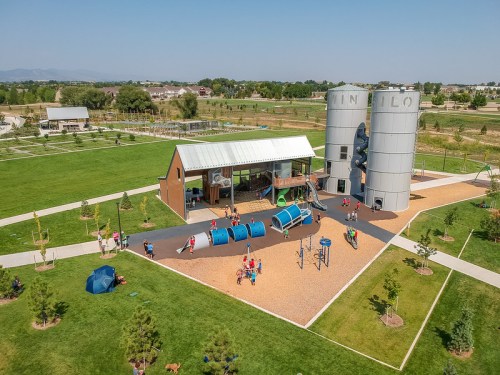 Aerial view of a playground with silos, featuring children playing on equipment and green fields in the background.