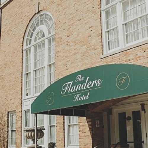 Exterior of The Flanders Hotel, featuring a green awning and large arched windows on a brick building.