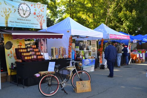 A vibrant market scene with vendor tents showcasing plant-based sauces, condiments, and various products.