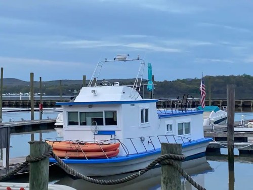 A white and blue boat docked at a marina, with kayaks on the deck and an American flag waving in the background.