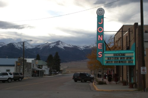 A small town street with a vintage theater sign reading "Jones," surrounded by mountains and cloudy skies.