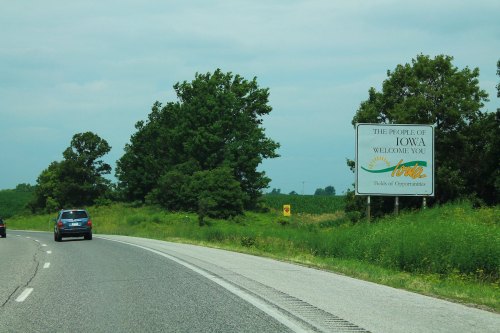 A highway sign welcoming travelers to Iowa, surrounded by green fields and trees.