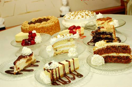 A variety of delicious cakes and desserts displayed on glass plates, including chocolate, carrot, and cheesecake.