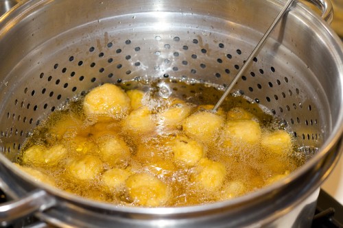 A pot of bubbling oil with small, round dough balls frying inside a perforated basket.