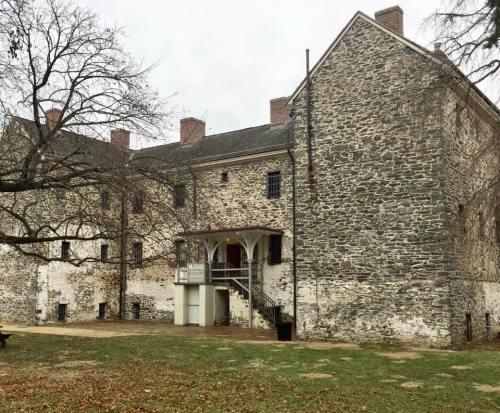 Historic stone building with multiple windows and a staircase, surrounded by bare trees and fallen leaves.