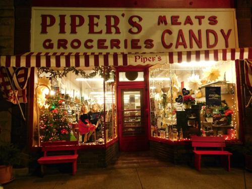 A festive storefront with "Piper's Meats, Groceries, Candy" sign, decorated for the holidays and featuring a Christmas tree.