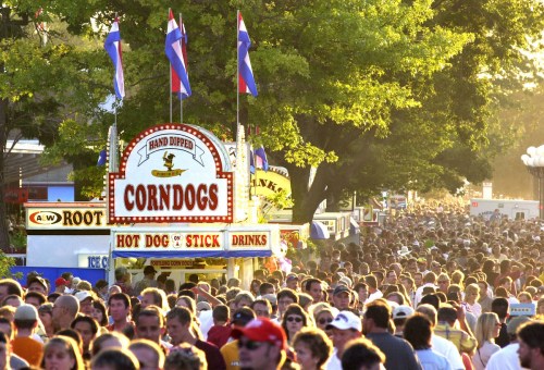 A bustling fair scene with a corndog stand and a large crowd of people enjoying the festivities.