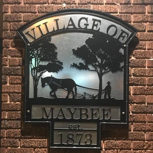 Sign for the Village of Maybee, established 1873, featuring a silhouette of a horse and plow with trees.