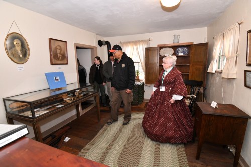 Two people explore a historical room filled with artifacts, including a display case and vintage furniture.