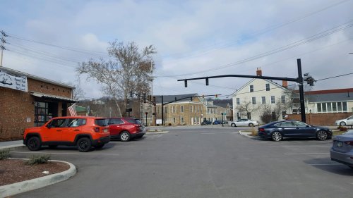 A view of a street intersection with parked cars, buildings in the background, and traffic lights overhead.