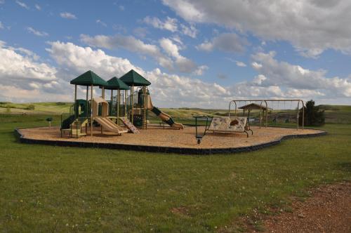 A playground with slides and swings on a grassy field under a cloudy sky.