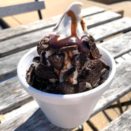 A cup of soft serve ice cream topped with crushed Oreos and drizzled with chocolate and caramel sauce.