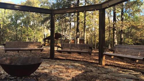 A serene outdoor space with wooden swings under a pergola, surrounded by trees and a fire pit in the foreground.