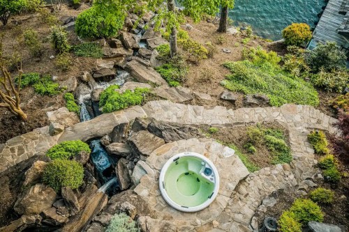 Aerial view of a landscaped garden with a hot tub, stone pathways, and a water feature near a lake.