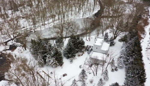 Aerial view of a snowy landscape featuring a house surrounded by trees and a frozen pond.