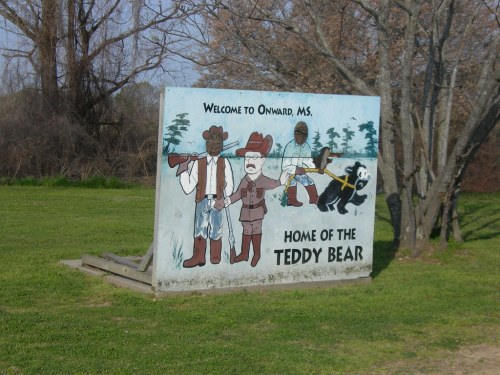 Sign welcoming visitors to Onward, MS, featuring a cartoon cowboy, a bear, and the text "Home of the Teddy Bear."